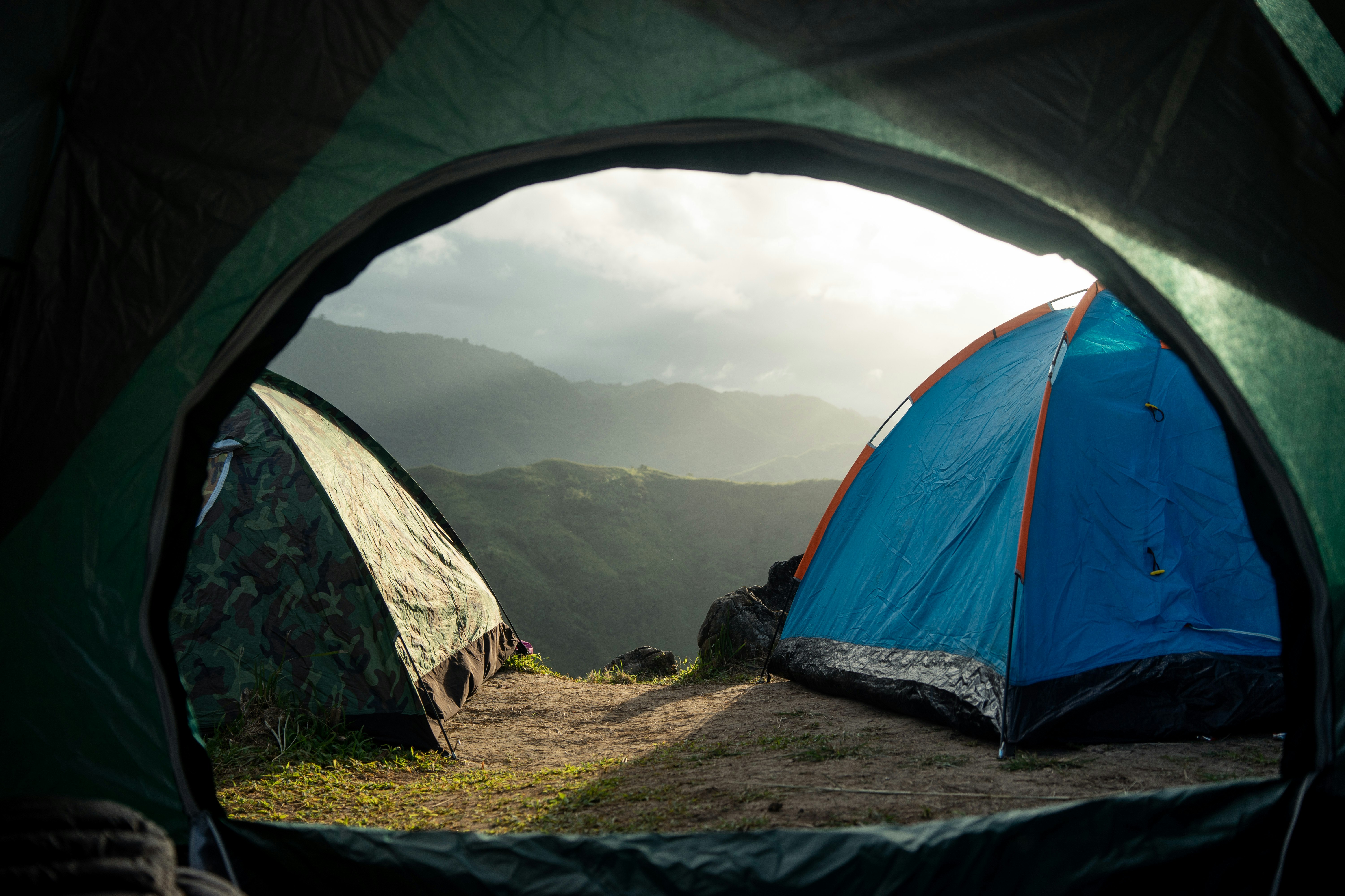 View from inside a tent looking out at two tents set up on grassy ground with mountains and a cloudy sky in the background | outdoorsurvivors com