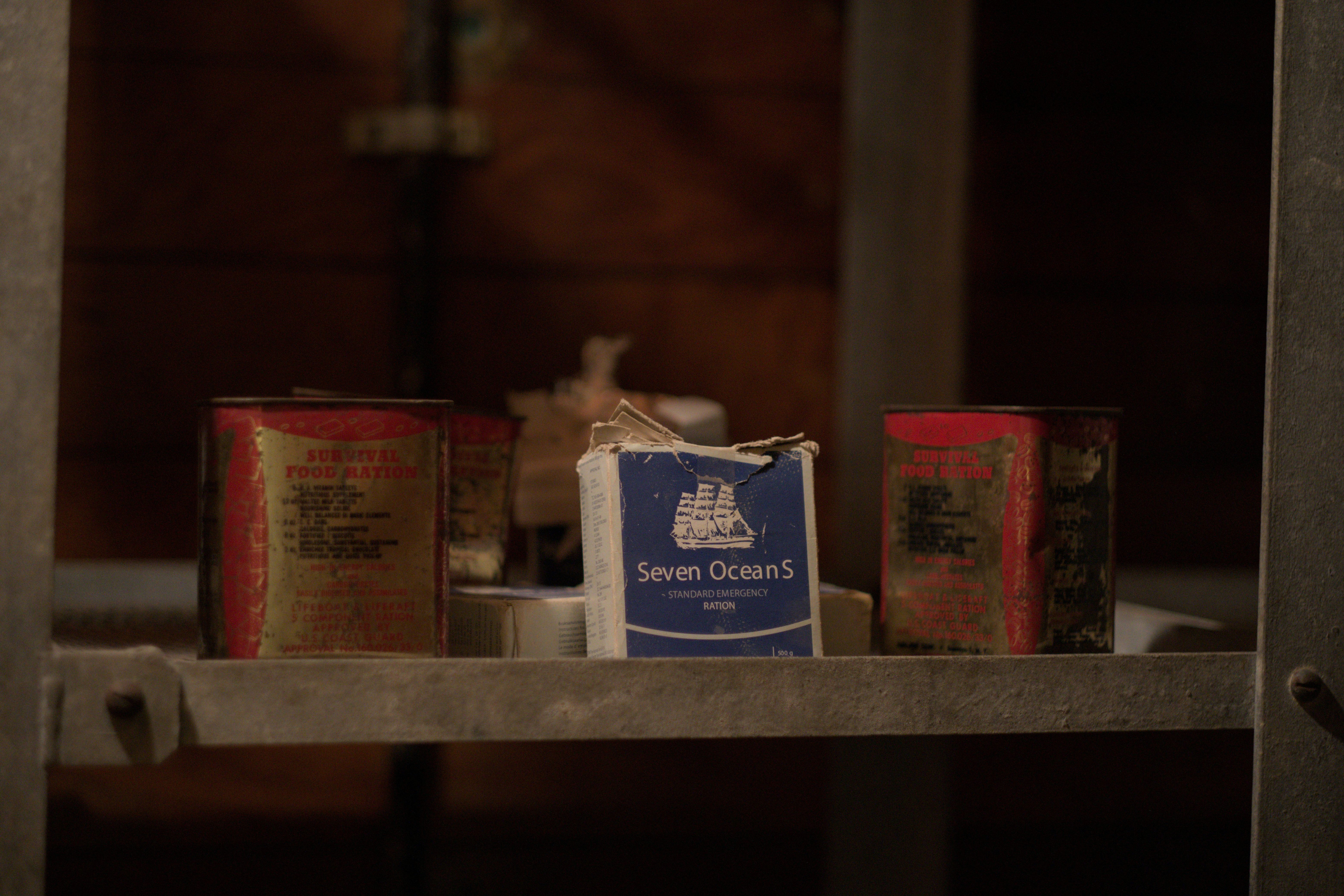 A box of Seven Oceans standard emergency ration flanked by two cans of survival food ration on a shelf | outdoorsurvivors com